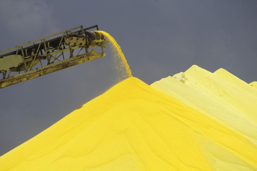 Large yellow sulphur stockpile beneath an industrial conveyor